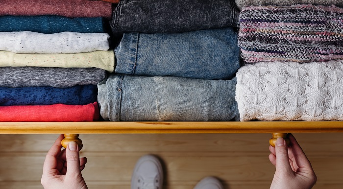 hands pulling out a clothes drawer to reveal perfecting folded and put away clothes. There's scarfs, jeans and a few tops all neatly folded.