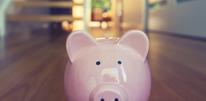 Pink piggy bank sitting on wooden floorboards in front of the stairs at home.