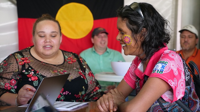 A financial counselor is helping an Aboriginal woman sort out her superannuation. In the background there is an Aboriginal flag.