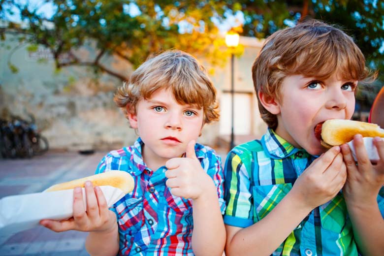 Two young boys eating a sausage in bread