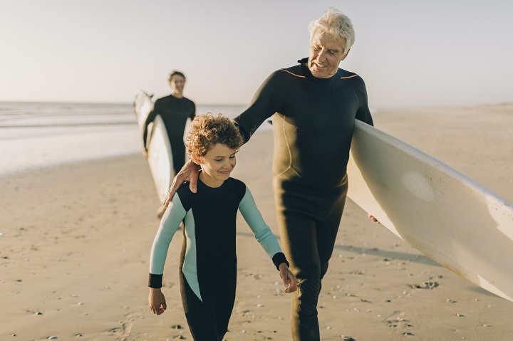 Grandpa with grandson walking on the beach with surfboards